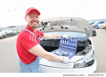 Portrait of young smiling car repairman with set of tools on hood of car 106238539
