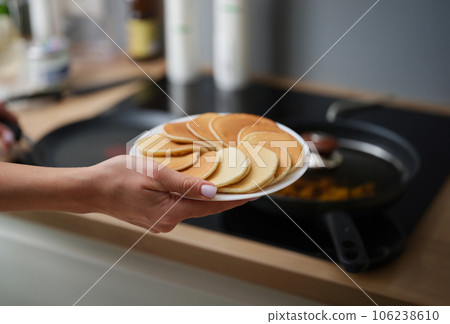 A woman's hand holds a white plate of pancakes 106238610
