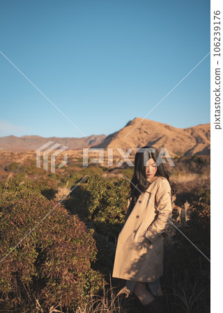一位女士手插在風衣口袋裡低頭看，背景是一座乾燥的山 106239176