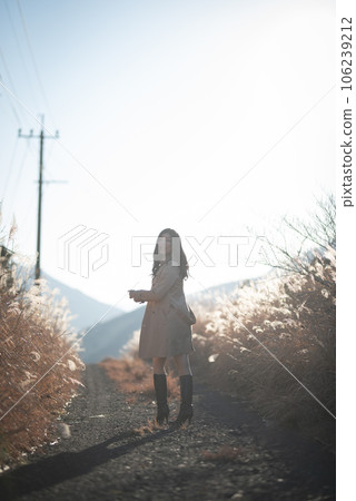 Back view of a woman walking while turning around on a gravel path between pampas grass Back view of a woman walking while turning around on a gravel path between pampas grass 106239212
