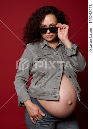 Pregnant woman dressed in casual jeans clothes, looking at camera, posing with naked belly, isolated studio background Pregnant woman dressed in casual jeans clothes, looking at camera, posing with naked belly, isolated studio background 106242068
