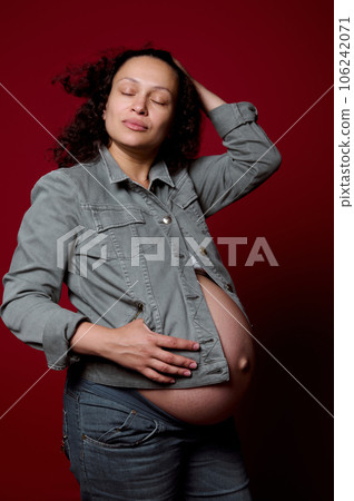 Beautiful pregnant woman wearing stylish casual denim blazer and jeans, posing over isolated red color studio background 106242071