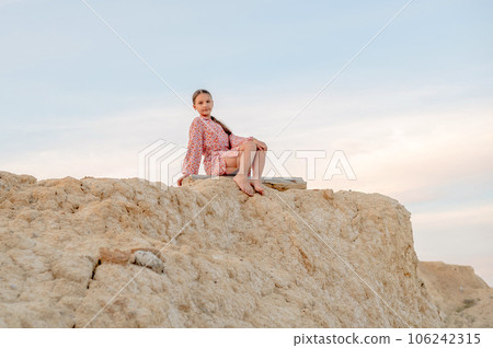 A girl sits on the edge of a cliff looking at the beauty of nature A girl sits on the edge of a cliff looking at the beauty of nature 106242315