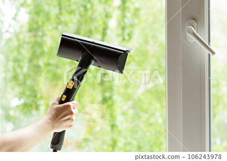woman washes the windows of a house with a steam generator. To clean up the house in the spring. House cleaning. 106243978