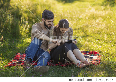 Young couple sitting in nature and looking at a tablet Young couple sitting in nature and looking at a tablet 106243987
