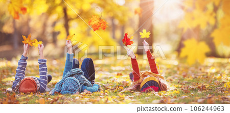 Children lying on the grass with maple leaves in their hands in autumnal park. Children lying on the grass with maple leaves in their hands in autumnal park. 106244963