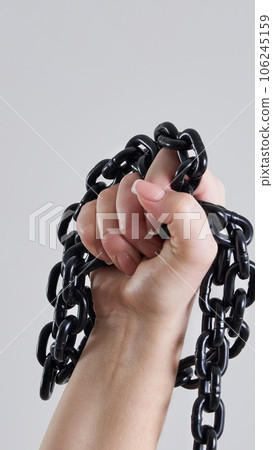 Female fist holding metal chain high up over grey background 106245159