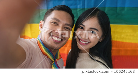 An attractive and cheerful Asian gay man enjoys talking while Selfie with his female friend a rainbow flag in the background 106245168