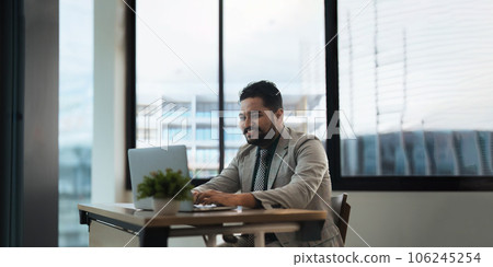 Indian businessman using laptop while analyzing reports in office 106245254