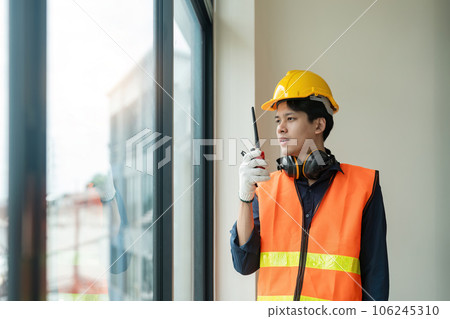 Asian male engineer standing at construction site and communicating with walkie talkie Asian male engineer standing at construction site and communicating with walkie talkie 106245310