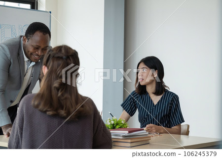 Positive friendly African American English tutor giving language courses to group of student of different and nationalities sitting around table in classroom 106245379
