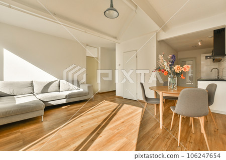 a living room with wood flooring and white walls, an open kitchen area in the corner is visible on the right side 106247654