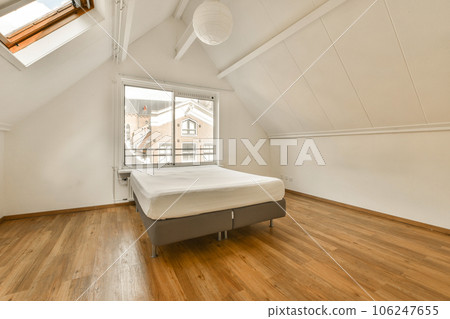 a bed in a room with wood floors and white paint on the walls, there is a window that looks out to the city 106247655