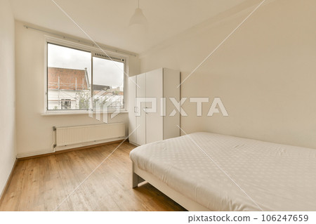 a bedroom with wood flooring and a white bed in front of a large window looking out onto the street a bedroom with wood flooring and a white bed in front of a large window looking out onto the street 106247659