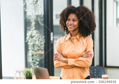 A beautiful young African American woman, smiling at the camera while standing with her arms crossed in a modern office. A beautiful young African American woman, smiling at the camera while standing with her arms crossed in a modern office. 106249838