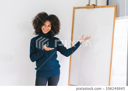 Studio portrait of Beautiful young African American woman smiling at camera pointing her finger at whiteboard. 106249845
