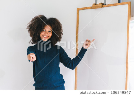 Studio portrait of Beautiful young African American woman smiling at camera pointing her finger at whiteboard. Studio portrait of Beautiful young African American woman smiling at camera pointing her finger at whiteboard. 106249847