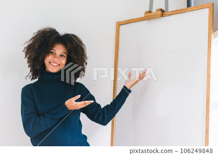 Studio portrait of Beautiful young African American woman smiling at camera pointing her finger at whiteboard. Studio portrait of Beautiful young African American woman smiling at camera pointing her finger at whiteboard. 106249848