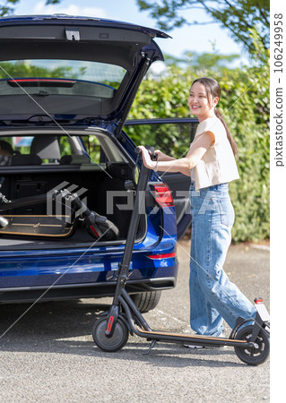 一位年輕可愛的女士在旅遊目的地停車場的汽車後備箱裡存放電動浮板 106249958