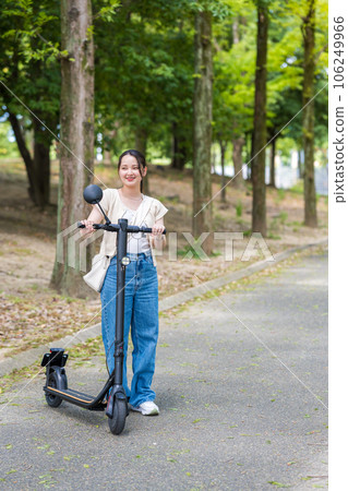 A young and cute woman refreshingly running on an electric kickboard on a beautiful green tree-lined street | Electric kickboard image A young and cute woman refreshingly running on an electric kickboard on a beautiful green tree-lined street | Electric kickboard image 106249966