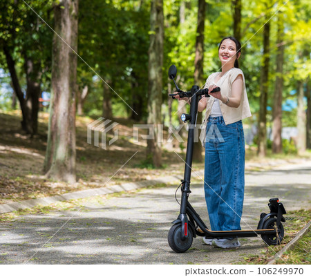 A young and cute woman refreshingly running on an electric kickboard on a beautiful green tree-lined street | Electric kickboard image 106249970
