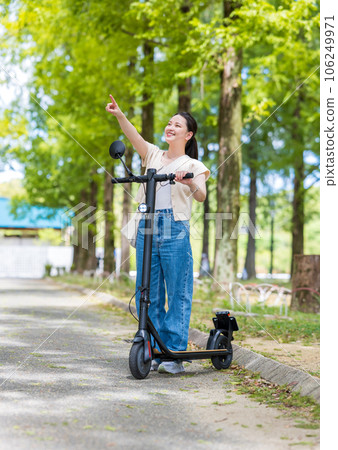 A young and cute woman refreshingly running on an electric kickboard on a beautiful green tree-lined street | Electric kickboard image 106249971