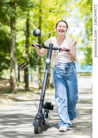A young and cute woman refreshingly running on an electric kickboard on a beautiful green tree-lined street | Electric kickboard image 106249973