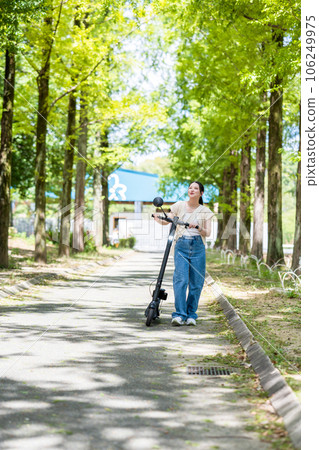A young and cute woman refreshingly running on an electric kickboard on a beautiful green tree-lined street | Electric kickboard image 106249975