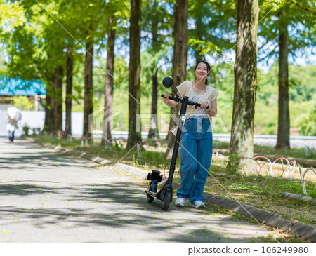 美麗的綠樹成蔭的街道上，一位年輕可愛的女士在電動滑板上清爽地奔跑 | 電動滑板圖片 106249980