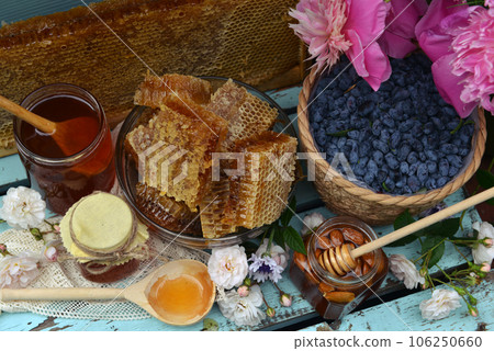 Still life with natural honey in jar, honeycomb cut in pieces and honeysuckle berry with peony on wooden background outside. Countryside summer rural background, vintage concept, healthy food Still life with natural honey in jar, honeycomb cut in pieces and honeysuckle berry with peony on wooden background outside. Countryside summer rural background, vintage concept, healthy food 106250660
