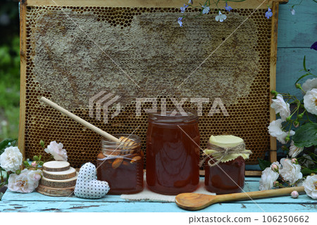 Still life with natural honey in jar, dipper, flowers and stick against background of honeycomb in frame outside. Countryside summer rural background, vintage concept, healthy food Still life with natural honey in jar, dipper, flowers and stick against background of honeycomb in frame outside. Countryside summer rural background, vintage concept, healthy food 106250662