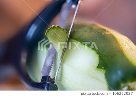 Selective focus on a vegetable peeler removing the outer skin of a cucumber 106252027