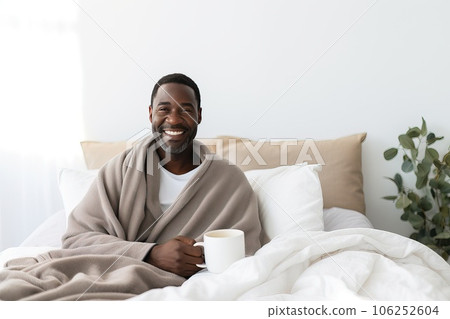 Smiling middle aged African American man with a cup of warm coffee in bed. 106252604
