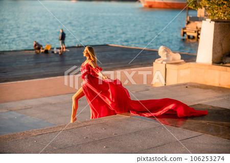 Sunrise red dress. A woman in a long red dress against the backdrop of sunrise, bright golden light of the sun's rays. The concept of femininity, harmony. 106253274