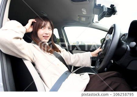 A young woman driving a car with an uneasy expression 106258795
