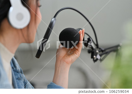 Side view of woman content creator in headphone talking through microphone for recording conversation for channel Side view of woman content creator in headphone talking through microphone for recording conversation for channel 106259034