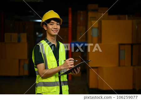 Male worker wearing safety hardhat and vest checking quantity of storage product on shelf in a large warehouse Male worker wearing safety hardhat and vest checking quantity of storage product on shelf in a large warehouse 106259077