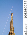 A spire and pinnacle sculptures of Milan Cathedral. Airplane leaving a line of cloud trail in the background. 106260077