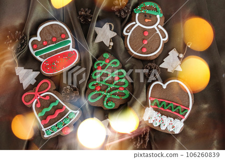 Banner for Christmas and New Year gingerbread. Christmas trees, toys, snowmen, garlands on a background of brown silk fabric. Bright bokeh. Banner for Christmas and New Year gingerbread. Christmas trees, toys, snowmen, garlands on a background of brown silk fabric. Bright bokeh. 106260839