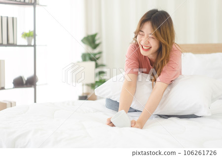 Portrait young adult asian woman sitting on bed with happy face after wake up in morning Portrait young adult asian woman sitting on bed with happy face after wake up in morning 106261726