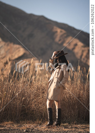 A woman in a trench coat standing with the dry mountains of Aso in the background A woman in a trench coat standing with the dry mountains of Aso in the background 106262022