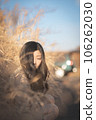 A black-haired woman crouching in pampas grass and looking down 106262030