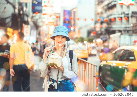 Young adult asian foodie woman backpack traveller eating coconut juice at china town street food. 106262045