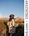 A woman looking into the distance with her hand in her trench coat pocket with a dry mountain in the background 106262549