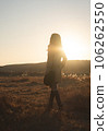A woman in a trench coat floating in the meadow in the sunset 106262550