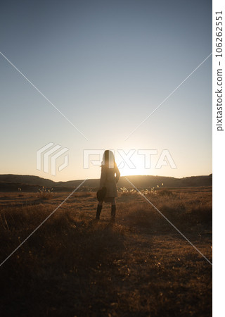 A woman in a trench coat floating in the meadow in the sunset 106262551