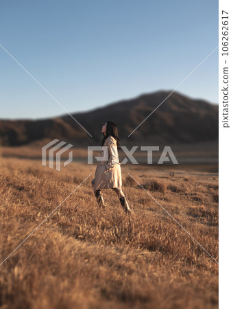 穿著風衣的女子沿著阿蘇草千里行走 穿著風衣的女子沿著阿蘇草千里行走 106262617