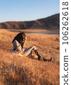 A woman sits on Kusasenri slope with one leg stretched and holding her hat with her hand 106262618