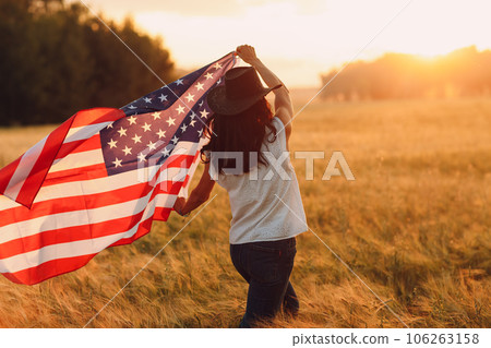 Woman with american flag on the field at sunset. Labor day concept. Woman with american flag on the field at sunset. Labor day concept. 106263158