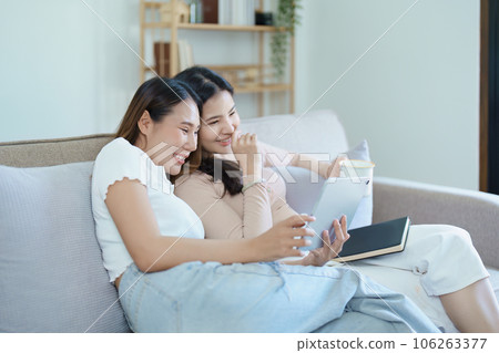 lgbtq, lgbt concept, homosexuality, portrait of two asian women posing happy together and loving each other while playing tablet at sofa. 106263377